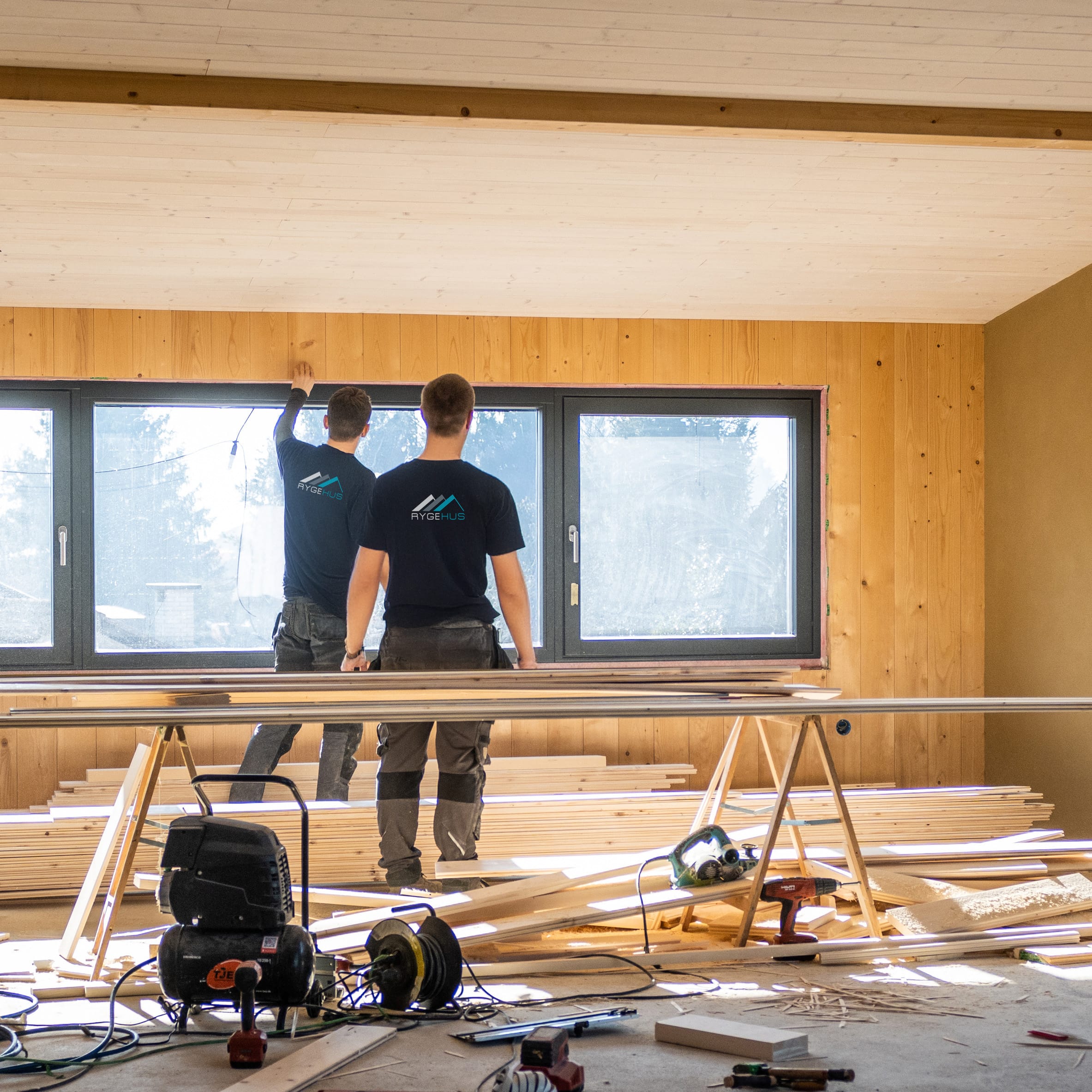 Workers making wooden lining of wall around window Back view of workers making wooden lining of wall around window. Building new modern house and working on construction site concept.